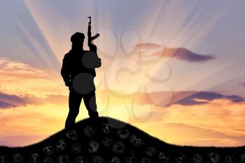 Concept of terrorism. Silhouette of a terrorist with a rifle standing on a pile of skulls at sunset