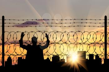 Silhouette of a man near the refugee fence of barbed wire on the background of evening city
