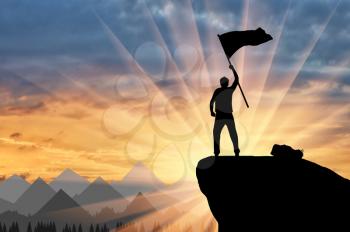 Silhouette of a climber on a mountain top with a flag in his hand. ?oncept of power and success