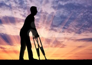Silhouette of a disabled man with crutches walking against the sunset. The concept of people with disabilities with crutches