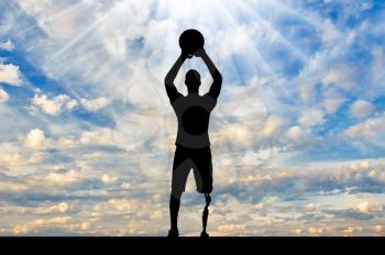 Silhouette of a disabled man with a leg prosthesis intends to throw a basketball ball. The concept of people with foot prosthesis and sport