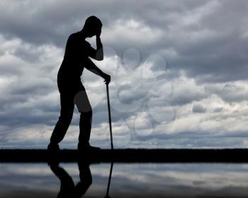 Silhouette of a sad disabled man with a cane in his hand by the river and his reflection. The concept of disabled people in depression
