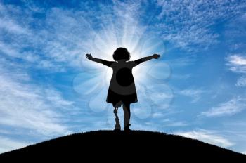 Happy disabled baby girl with prosthetic legs outdoors on sky background. The concept of happy childhood of children with prosthetic legs