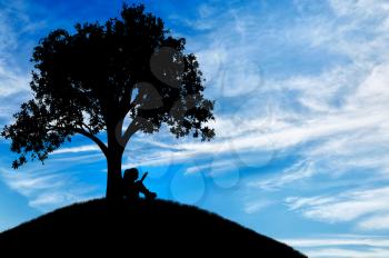 Silhouette of a little girl reading a book under a tree. Conceptual image of childhood