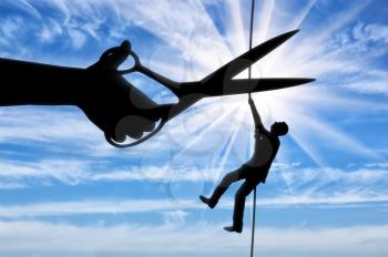 Silhouette of a businessman climbs on a tightrope and a hand with scissors intends to cut a rope. The concept of a rival in business
