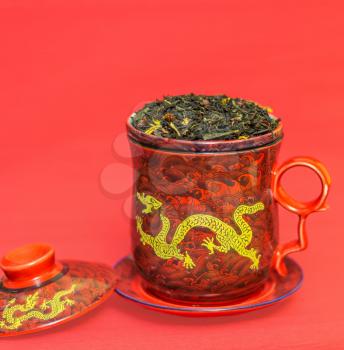 Beautiful red tea mug with a gold dragon on a red background. Shallow depth of field, focus on tea leaves.