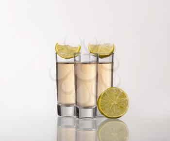 Three gold tequila shots with lime  on white background