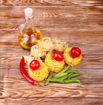 Pasta on the wooden background with tomato, lettuce pepper, olive oil and pepper