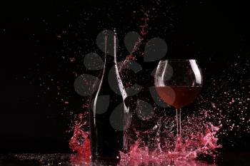 bottle with red wine, water splash, wine on table on black background, big splash around bottle of red wine 