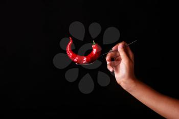 Fork impale to red hot chili on black background.  woman's hand holding a fork