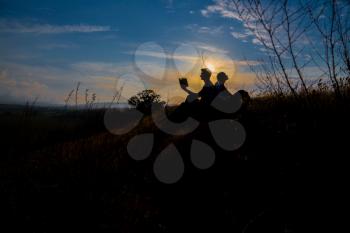 Man and woman reading in the park against sunset. Silhouette of couple reading book at sky sunset . warm tone and soft focus. Concept of love