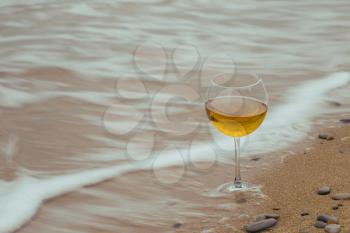 Romantic glass of wine sitting on the beach, overcast autumn weather, cold wind
