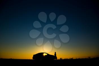 Silhouette of sedan car with girl on the background of beautiful sunset