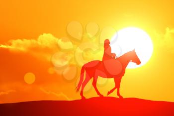 Silhouette or woman and horse running across horizon as the sun goes down.