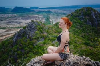 Active healthy lifestyle concept. Happy female hiker sitting on a cliff in relax pose and feeling free. Khao Daeng View Point, Thailand