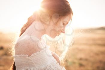 red-haired girl in a field of wheat in a white dress smiles a lovely smile , a perfect picture for advertising in the style lifestyle. beautiful cinematographic picture at sunset