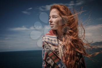 Gorgeous Romantic Girl Outdoors. Beautiful Model near sea. Long Hair Blowing in the Wind. Red-haired girl in ethnic costume on the ocean coast