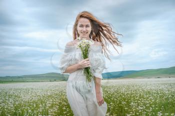Beautiful young girl with curly red hair in chamomile field. Concept and idea of a healthy lifestyle, skin and hair care