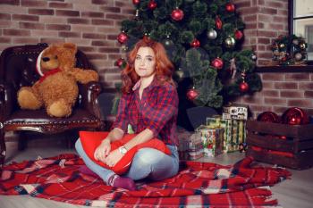 Christmas Gift. New year celebration. Beautiful holdiay decorated room with Christmas tree with presents under it. New Year and Christmas concepts. Beautiful girl sitting near New Year tree.