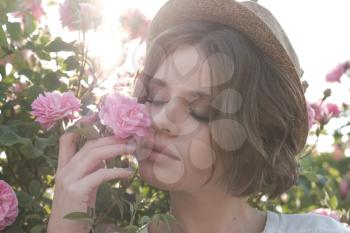 Beautiful young woman with curly hair posing near roses in a garden. The concept of perfume advertising.