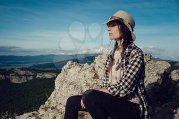 woman traveler with backpack holding hat and looking at amazing mountains and forest, wanderlust travel concept, space for text, atmospheric epic moment