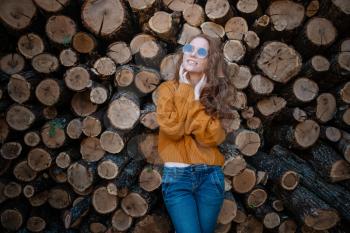beautiful amazing gorgeous redhair girl spins in yellow sweater, jeans and glasses on the background of firewood. Autumn mood