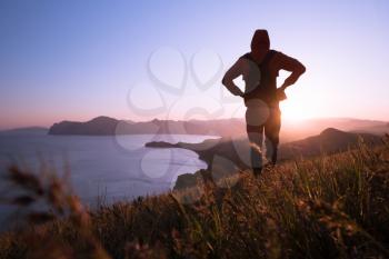 Young standing man with backpack. Hiker on the stone on the seashore at colorful sunset sky. Beautiful landscape with sporty man rocks sea and clouds at sunset. Sporty lifestyle