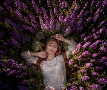 woman with purple flowers. Beautiful red-haired girl in a flourishing field enjoying freedom and rest