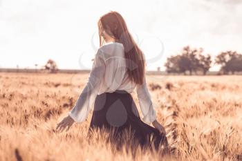 Red-haired girl in a wheat field at sunset. Beautiful woman in golden field at sunset, Backlit warm tones