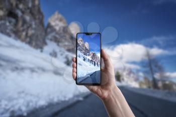 A man makes a photo on a smartphone, beautiful landscape of Scenic winter view from the asphalt road in the mountains covered with snow of South Tyrol, North of Italy, Gardena Pass