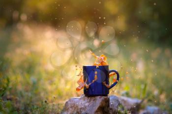 Blue mug of hot tea or coffee with milk, outdoor, the concept of travel, spray, splash. Glare on the pictures from the setting sun, pleasant bokeh