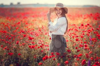Young beautiful woman walking and dancing through a poppy field, summer outdoor. Toned.