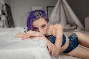 Charming sexy woman in lingerie lying on the bed in the room. purple hair and dark blue underwear