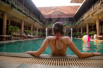 Beautiful women relaxing at the luxury poolside. Girl at travel spa resort pool. Summer luxury vacation. Hotel in traditional Thai style, rest in exotic. view from the back