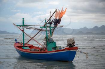 Thai long tail boat during low tide in ocean with carst mountains in background and cloudscape at Thailand, Asia