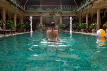 Beautiful women relaxing at the luxury poolside. Girl at travel spa resort pool. Summer luxury vacation. Hotel in traditional Thai style, rest in exotic. view from the back