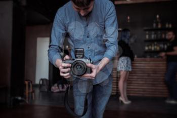 Close-up of hand holding camera. Mirrorless camera close up in the hand of a young man on a studio background. The reporter's taking a picture. the photographer looks into the camera.