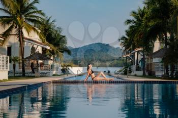 summer holidays in luxury hotel, woman relaxing near beautiful swimming pool. Beauty and body care. Back view, without face