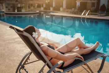 Happy young woman in swimsuit laying on chaise-longue poolside. The concept of a summer holiday.