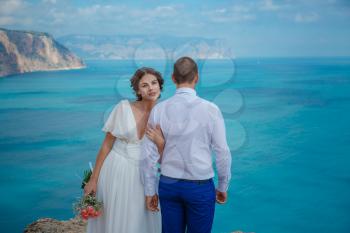 Beautiful smiling young bride and groom walking on the beach, kissing and having fun, wedding ceremony near the rocks and sea. Wedding ceremony on coast of Cyprus