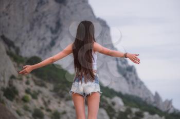 Beautiful young woman travels through a mountainous area. The concept and idea of a summer holiday, hitchhiking, finding your own way