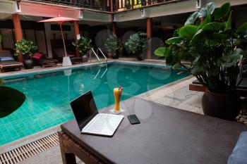 A white laptop, smartphone and mango smoothie on a sunbed against swiming pool background. A start of new day. Freelance business concept. Flexible remote working, travelling, advert and copy space