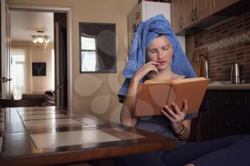 Young asian woman after bath in towel reads a book in the kitchen. Natural beauty healthy model happy enjoying self isolation. stay at home social media campaign for coronavirus prevention