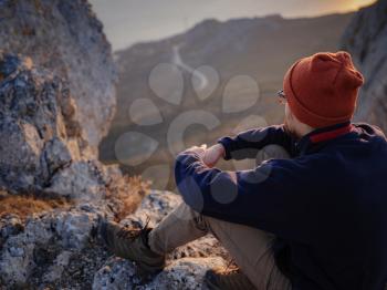 A young man standing on top cliff in spring mountains at sunset and enjoying view of nature. Mountain and coastal travel, freedom and active lifestyle