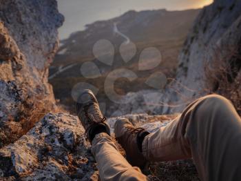 Close Up view on male feet wearing hiking boots. Man tourist sitting on the edge cliff mountains above sea