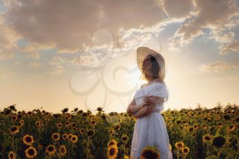 Beautiful young girl enjoying nature on the field of sunflowers at sunset. beautiful back sunset light. Asian girl in a cute white dress and hat enjoys summer and vacation.