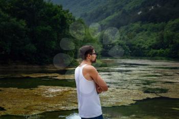 The young male hipster looking at the beautiful view at the lake. Beautiful freedom moment and peaceful atmosphere in nature. Back view.