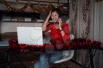 attractive asian woman with gift box taking a call against cozy decorated room. she calling family for traditional good wishes