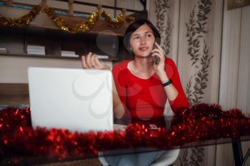 attractive asian woman with gift box taking a call against cozy decorated room. she calling family for traditional good wishes