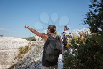 Two Hikers with Backpacks and other climbing Gear staying on top of Rock. man pointing with his hand discussing route. Plan, vision and mission concept.